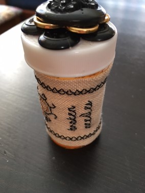 pill bottle with embroidered sleeve and buttons decorating cap
